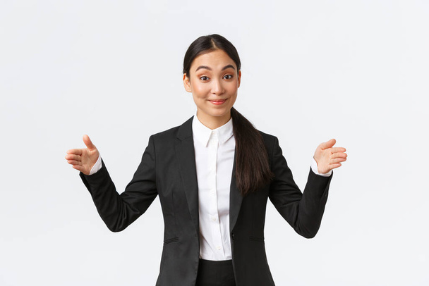 Усміхнена приємна азіатська бізнес-леді, продавчиня в чорному костюмі намагається щось продати, формує великий об'єкт, вводить продукт клієнту, має бізнес-презентацію проекту, білий фон
 - Фото, зображення