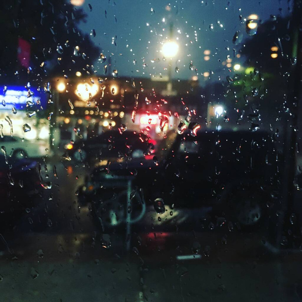 Dívat se z dešťového okna baru do komerčních obchodů a rušné ulice v Queensu v New Yorku. Noční světlo prosvítající oknem zakrytým kapkami deště během silné dešťové bouře, filtrováno - Fotografie, Obrázek