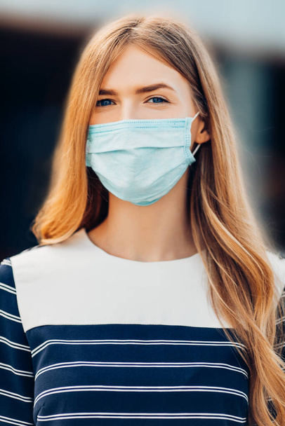attractive young woman in a medical protective mask on her face, standing in the city against the background of a building. Quarantine, coronavirus, - Fotó, kép
