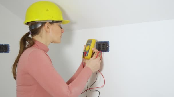 CERRAR: Mujer joven electricista inspecciona dos tomas de corriente mediante el uso de un voltímetro. - Metraje, vídeo