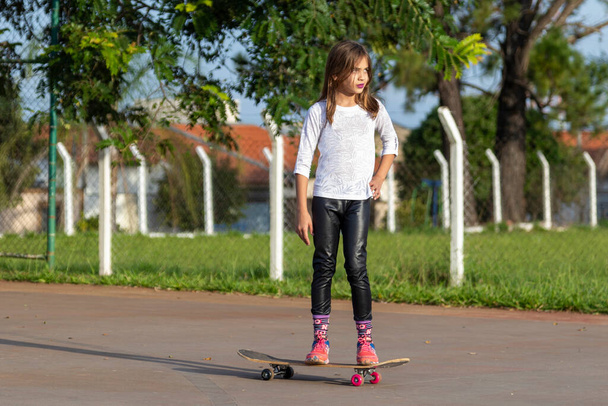 Menina loira bonita montando um skate no parque ao pôr do sol
. - Foto, Imagem