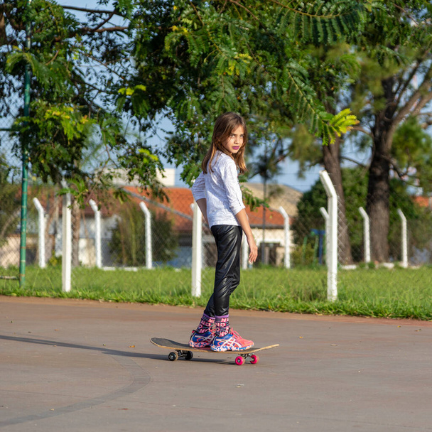 Mooi blond meisje paardrijden een skateboard in het park bij zonsondergang. - Foto, afbeelding