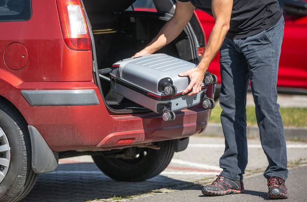 Padre cargando un equipaje al coche, preparándose para unas vacaciones o vacaciones en el extranjero, concepto de transporte
 - Foto, imagen