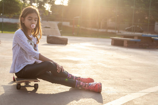 Krásná blondýna dívka sedí na vrcholu skateboardu v parku při západu slunce. - Fotografie, Obrázek