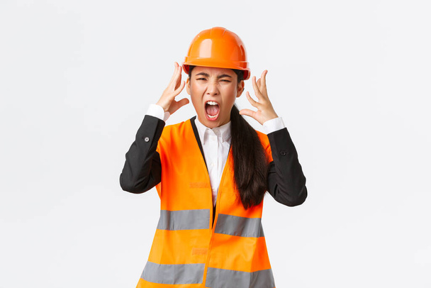 怒り狂ったアジア系女性のチーフエンジニア建設管理者は激怒し、従業員の怒りを失い、手を積極的に叫び、握手し、誰かを叱りつけるように激怒しました - 写真・画像