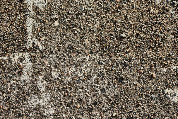 Teile der alten Markierungen auf dem Asphalt sind durch die Steine der kaputten Straße sichtbar  - Foto, Bild