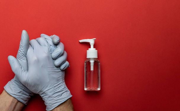 Antiseptic hand using antibacterial sanitizer gel in lab gloves. Clear sanitizer in pump bottle. Medical red background for corona virus prevention, hygiene to stop spreading coronavirus - Photo, Image