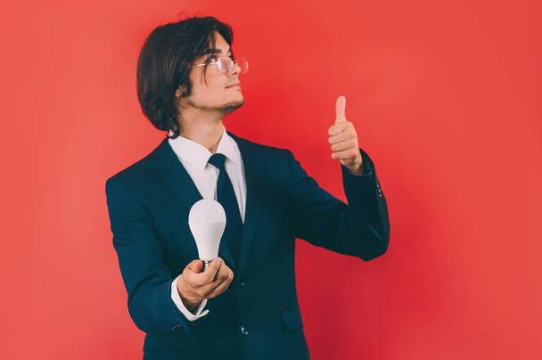 Businessman with a light bulb in his hands, on a red background. Concept on the topic of ideas - 写真・画像