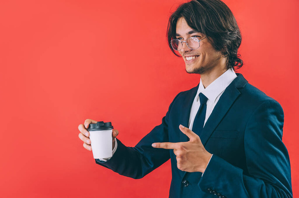 Businessman with a cup of coffee in his hands on a red background - Фото, изображение