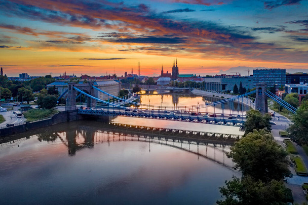 Drone uitzicht op de Grunwaldzki brug boven Oder rivier in Wrocaw bij prachtige zonsondergang. Spoedig verkeer, verlichte historische gebouwen en bruggen. Prachtige lucht, lichte reflecties op het wazige water - Foto, afbeelding