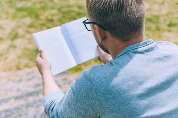 The guy reads a book outdoors on a background of grass - Photo, Image