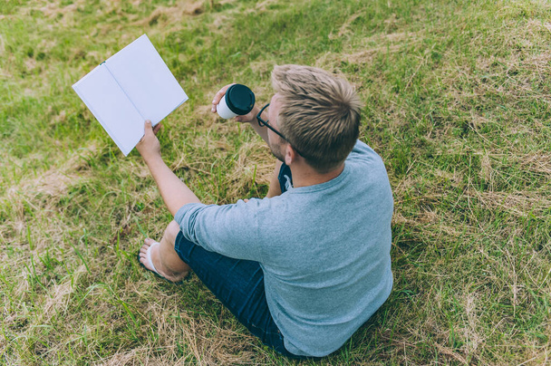 O tipo com uma chávena de café lê um livro ao ar livre
 - Foto, Imagem