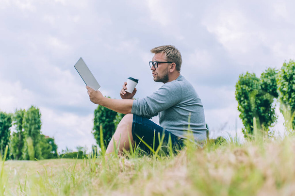 El tipo con una taza de café lee un libro al aire libre
 - Foto, imagen