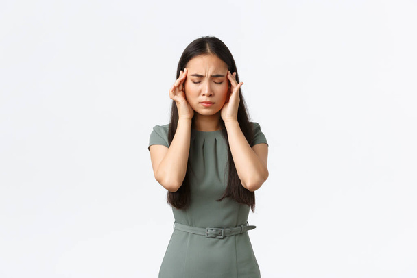 Propriétaires de petites entreprises, femmes entrepreneurs concept. Femme asiatique épuisée en robe se sentant malade, les yeux fermés et les tempes touchantes, souffrant de maux de tête douloureux, ayant la migraine - Photo, image