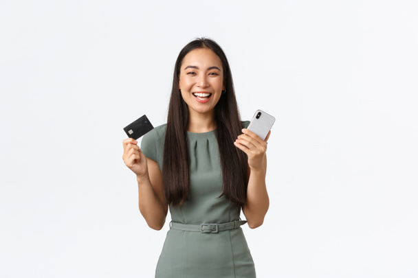 Власники малого бізнесу, концепція жінок-підприємців. Щаслива азіатська бізнес-леді, яка використовує інтернет-банкінг, розміщує готівку на депозит, тримає мобільний телефон і кредитну картку, купуючи онлайн
 - Фото, зображення