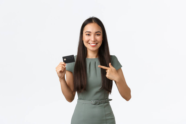 Small business owners, women entrepreneurs concept. Smiling attractive businesswoman, bank clerk in dress, pointing finger at credit card, promote new service, finance app, white background - Photo, Image