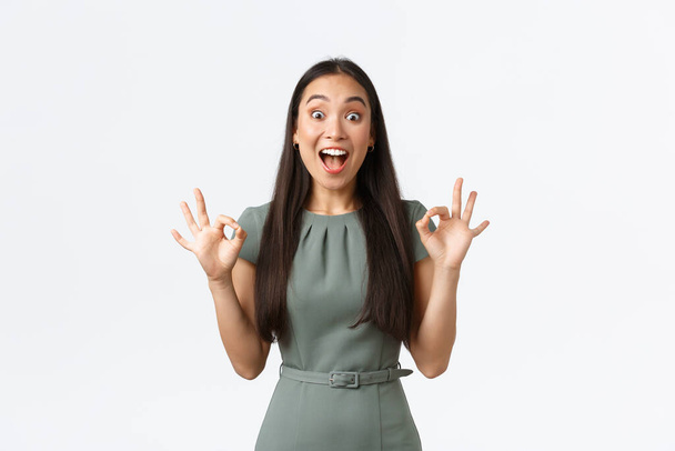 Small business owners, women entrepreneurs concept. Excited happy asian woman looking pleased and extremely thrilled, showing okay gesture and smiling astounded, white background - Fotó, kép