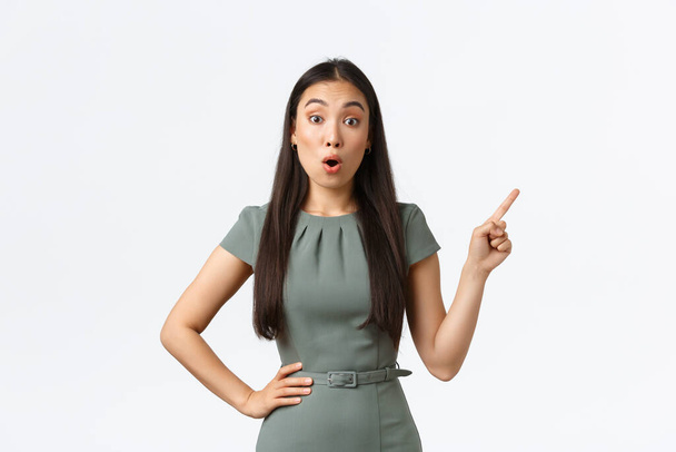 Small business owners, women entrepreneurs concept. Surprised and amazed asian businesswoman asking question about product, pointing finger upper right corner and look astounded - Photo, Image