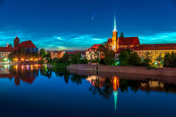 Longo período cometa NEOWISE e nuvens noctilucent (NLC) visto acima de Wroclaw na Polônia. Noite bonita brilhando nuvens com raro astrônomo fenomeno sobre a cityline. O céu reflete no rio Oder
 - Foto, Imagem