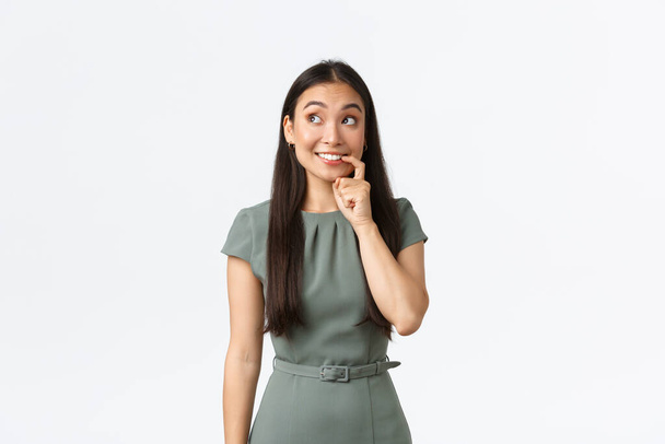 Small business owners, women entrepreneurs concept. Tempting and excited cute asian woman biting finger and looking with desire, thinking, making decision, standing white background - Photo, Image