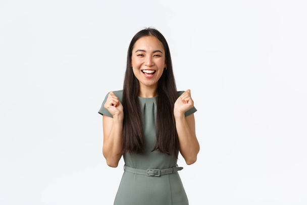 Kleinunternehmer, Unternehmerinnen. Aufgeregt glückliche asiatische Frau im Kleid, Geschäftsfrau, die gewinnt oder ein Ziel erreicht, Faustpumpe als Siegesfeier, triumphierend über weißem Hintergrund - Foto, Bild