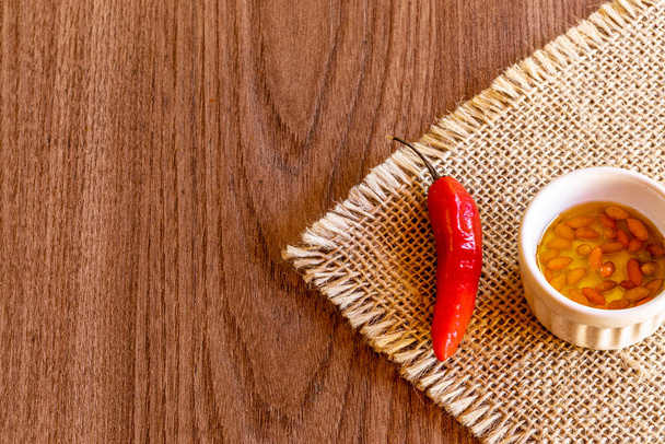 Small bowl with oil and pepper on rustic wooden background. - Photo, Image