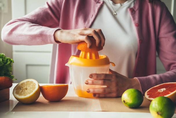 close-up foto van een blanke vrouw met gezonde gewoonten knijpen sap van sinaasappels en citroenen in de keuken - Foto, afbeelding