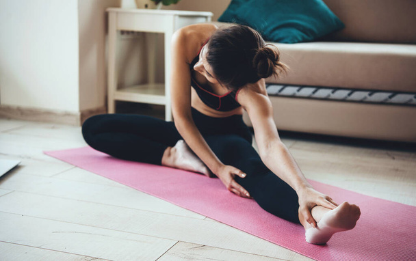 Genç beyaz kadın evde yoga yapmadan önce esneme hareketleri yapıyor ve spor kıyafetleri giyiyor. - Fotoğraf, Görsel
