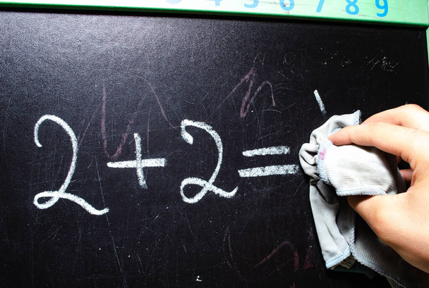 School bestuur. Het bord waarop het alfabet is geschreven, nummers, een voorbeeld van optellen. Veeg het bord af met een doek. Vingers van een hand in krijt van een schoolbestuur - Foto, afbeelding