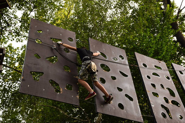 Jovem corre um curso de obstáculos de árvore em árvore em um parque de corda
 - Foto, Imagem