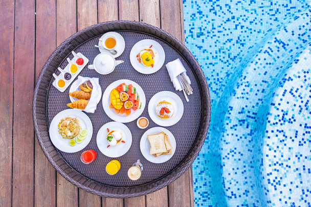 Επιπλέοντας δίσκο πρωινού γύρω από εξωτερική πισίνα με ψωμί φρούτα αυγό φλιτζάνι καφέ και χυμό - Φωτογραφία, εικόνα
