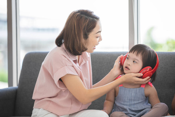 Маленька дівчинка з обмеженими можливостями навчання або група синдрому Дауна слухає музику з навушників з викладанням матері та заохоченням поруч.
. - Фото, зображення