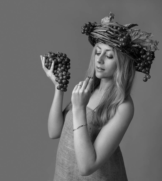 Portrait of  beautiful caucasian blonde woman with grapes. Shy image of a blonde nymph in a wreath of vines, grapes and dry leaves. Black and white. - Foto, Imagem