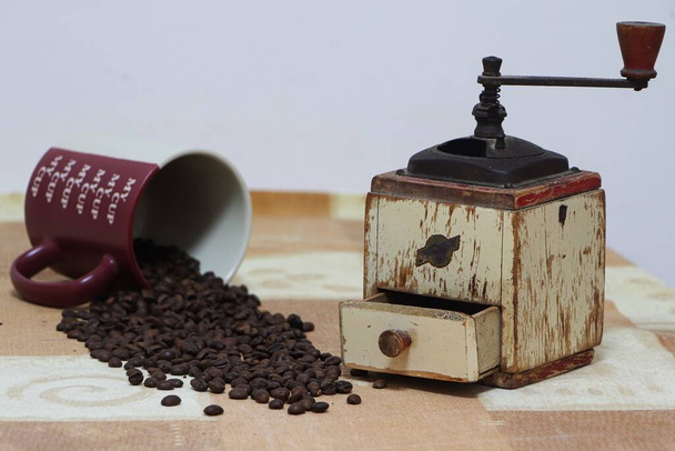 Zátiší kávových zrn na stole se starožitným mlýnkem na kávu a hrnečkem - Fotografie, Obrázek