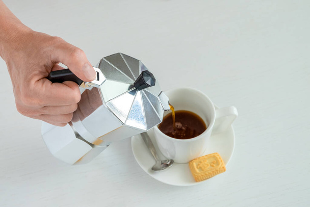 Жіноча рука тримає гейзерну кавоварку. Чорна гаряча кава вливається в білу порцелянову чашку. Горизонтальна орієнтація, вибірковий фокус
. - Фото, зображення