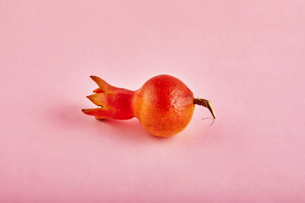 Mini granaatappel liggend op een roze achtergrond met een schaduw. - Foto, afbeelding