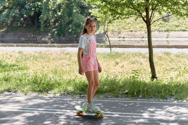 A girl in a pink jumpsuit is riding a snowboard in the park. Summer holidays. - Fotoğraf, Görsel