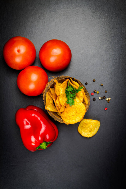 Potato chips red bell pepper and three tomatoes. Black background - Foto, immagini