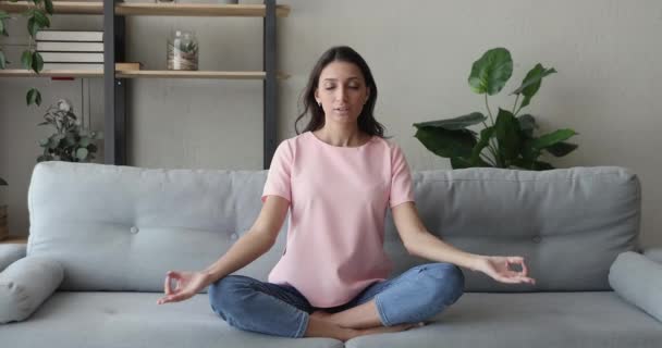Indian woman meditating sitting in lotus position on couch - Πλάνα, βίντεο