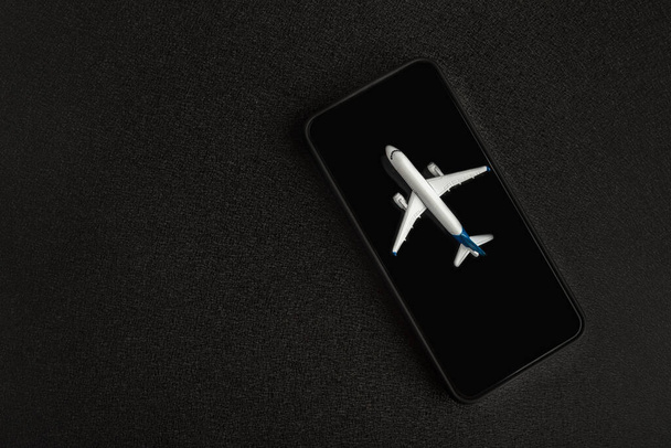 Modell repülőgép okostelefonon, fekete háttér. Repülőjegy-keresés iránti kérelem - Fotó, kép