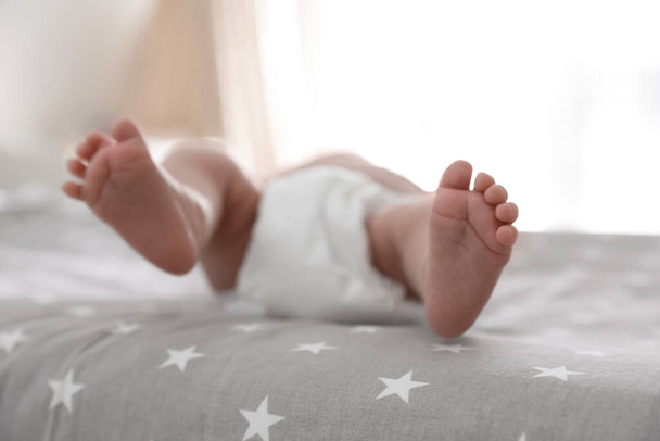 Cute little baby in diaper lying on bed in room, closeup - Foto, Bild
