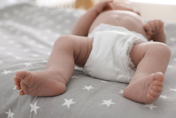 Cute little baby in diaper lying on bed in room, closeup - Fotografie, Obrázek