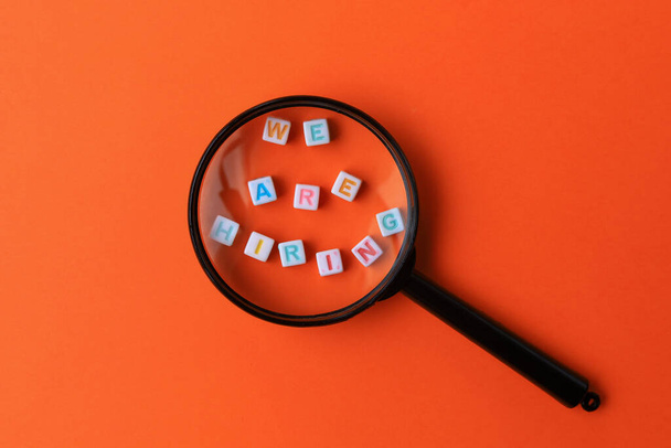 Text or inscription We are hiring. Cubes with letters under a magnifying glass on an orange background with copyspace. HR concept. - Foto, Imagem