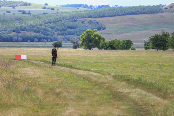 Un militare con un walkie-talkie in un campo verde. Vista da una distanza dal retro. Sfondo militare astratto. - Foto, immagini
