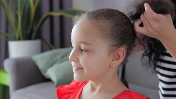 Mom of a happy family, a loving European at home on the couch doing hairstyle, combing the hair of his little cute daughter, the child rejoices at papas concern for her. - Imágenes, Vídeo