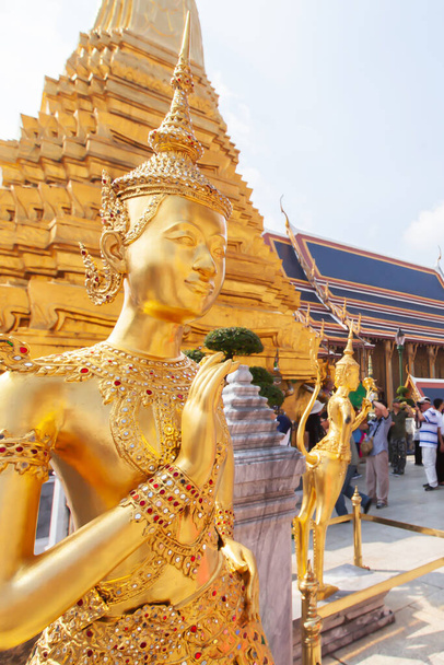 Elegant golden Kinnari statue at Grand Palace, Bangkok, Thailand, A group of tourists appreciating the Grand Palace in the backgrounds. The Grand Palace is open to the public. - Фото, зображення