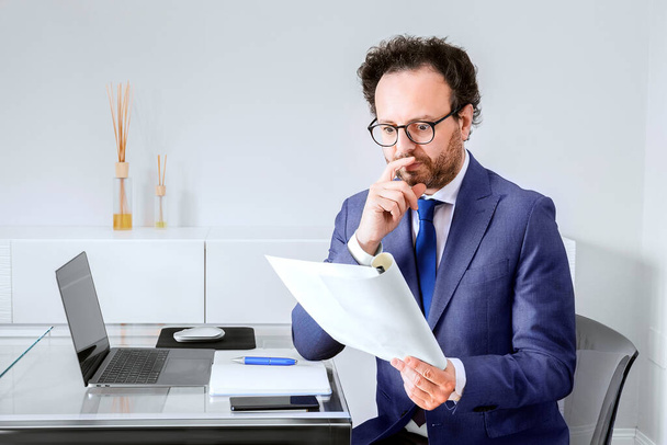 Shocked european businessman in business suit holding analytical report document on home office interior backdrop. The concept of bankruptcy, the economic crisis - Фото, изображение