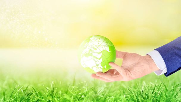 Businessman holding Planet Earth in hand against green grass meadow in sunshine. Concept of ecology, environment, global business - Photo, Image