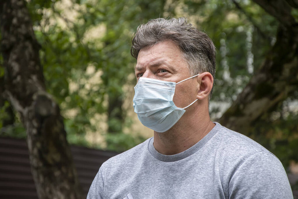 Ritratto di strada di un uomo di 40-45 anni con una maschera medica sullo sfondo della natura.Uno sguardo serio è diretto a lato.. - Foto, immagini