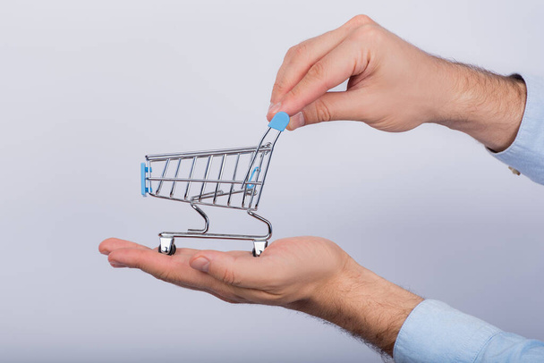 Male hands holding small shopping cart on white background. Side view. - Foto, Imagem
